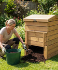 Woman using Solid Wood Compost Bin 48 Gallon Outdoor Bin With Lockable Sliding Door Flip Top Opening Gas Rods in a garden