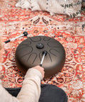 Person playing Super Responsive 16 Inch Steel Tongue Drum With Eight Soothing Notes on a rug with pro grip mallets.