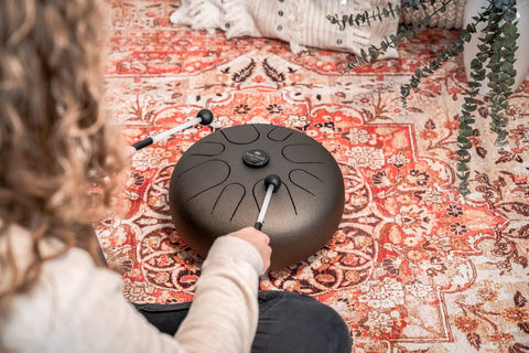 Person playing Super Responsive 16 Inch Steel Tongue Drum With Eight Soothing Notes on a rug with pro grip mallets.