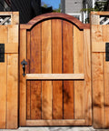Wooden garden gate with vertical planks and black metal hardware, surrounded by wooden fence panels and trellis.