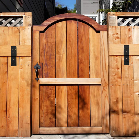 Wooden garden gate with vertical planks and black metal hardware, surrounded by wooden fence panels and trellis.