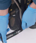 Person applying Aquaseal SR Shoe Repair Adhesive to hiking boot sole with gloves for fixing and sealing holes and leaks.