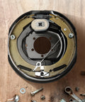Electric trailer brake assembly backing plate inner view; 12x2 in, metal brake shoes and springs.