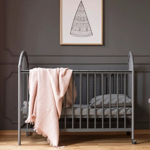 Gray crib with pink blanket hanging, modern room decor.