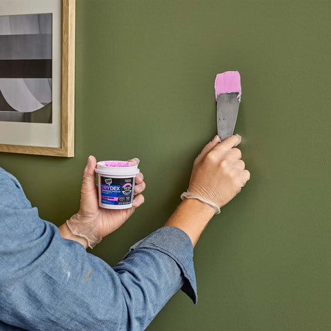 Applying Dry Time Indicator Spackling For Fast DIY Repairs Pink When Wet Dries White In 1 To 5 Hours 8 Oz on green wall