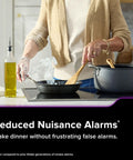 Person cooking in a kitchen with app enabled hardwired smart smoke and carbon monoxide detector with AA battery backup nearby