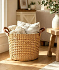 Large Water Hyacinth Storage Basket 15.7 Inch woven seagrass bin with sturdy design, filled with blankets and cushions, next to a sofa.