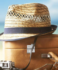 Straw hat and vintage suitcase by the beach with an old camera and leather straps, highlighting a relaxed travel vibe.