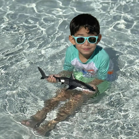 Child in sunglasses holding Remote Control Shark Pool Toy For Kids With Lights And Water Spray 2.4GHz, Dual Motors in pool