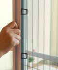 Hand using a 30 Piece Tough As Nails Black Plastic Window Screen Pull Tab for Universal Spline Channel Repair on a window.