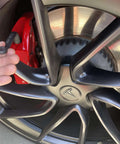 Close-up of a car wheel with a hand holding a part from the 3 Piece 11mm Offset Brake Bleeder Wrench Set For Audi BMW VW Caliper Mounted Electromechanical Parking Brake Compatible No Wheel Removal Easy To Use Great For DIYers