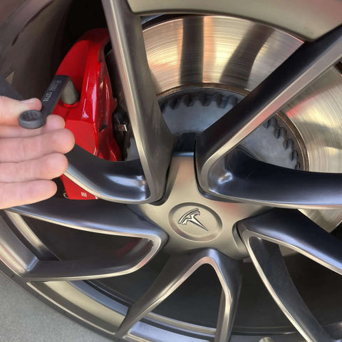 Close-up of a car wheel with a hand holding a part from the 3 Piece 11mm Offset Brake Bleeder Wrench Set For Audi BMW VW Caliper Mounted Electromechanical Parking Brake Compatible No Wheel Removal Easy To Use Great For DIYers