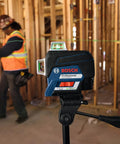 Boss Class 12V Max Three Plane Green Beam Laser Level on stand in construction site, with contractor using laser for alignment.
