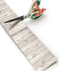 White Wood Rolled Border Trim 50ft For Bulletin Boards And Classrooms being cut with scissors, showing texture