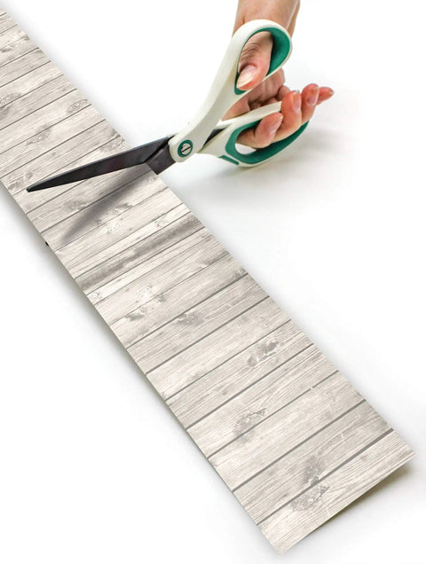 White Wood Rolled Border Trim 50ft For Bulletin Boards And Classrooms being cut with scissors, showing texture