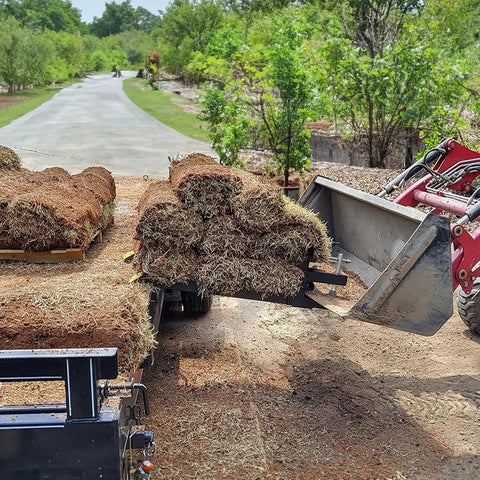 Heavy Duty 42 Inch Clamp On Debris Forks for Skid Steer With 2500 Lbs Capacity lifting grass rolls on a dirt road