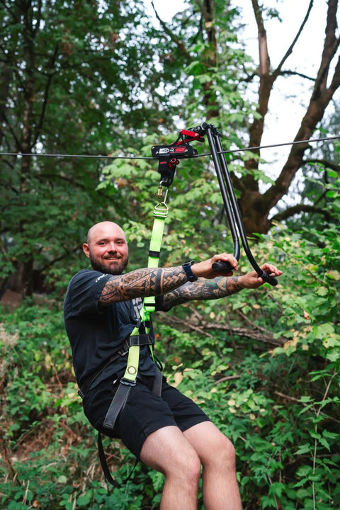 Person using All In One Zip Line Trolley Pro X With Brake Bundle in forest setting, showing harness and cable connection.