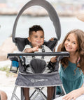 Toddler sitting in Go With Me Venture Portable Toddler Chair On The Go With Sun Canopy For Indoor And Outdoor Use, beach setting