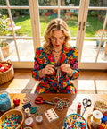 Woman crafting jewelry with beads at a sunlit table, surrounded by crafting materials and tools.
