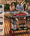 Foldable Grill Cart With Oversized Wheels For 17 To 22 Inch Grills in use at a backyard gathering, showing cooking surface and storage space