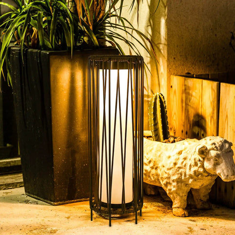 Outdoor Solar Floor Lamp With Rattan Trim And Steel Frame, Waterproof Patio Lantern next to plants and sculpture