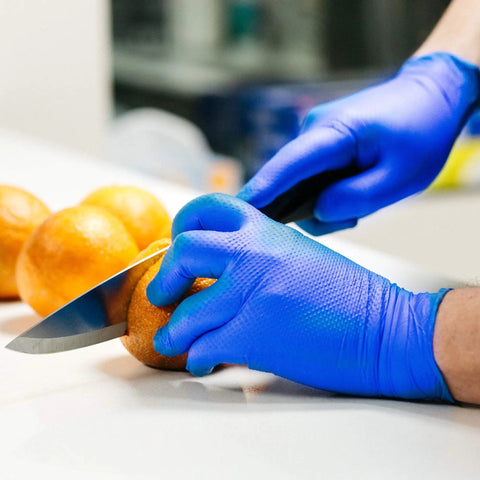 Person wearing HD Royal Blue Nitrile Industrial Disposable Gloves Heavy Duty 6 Mil Thick Latex Free With Raised Diamond Texture slicing orange
