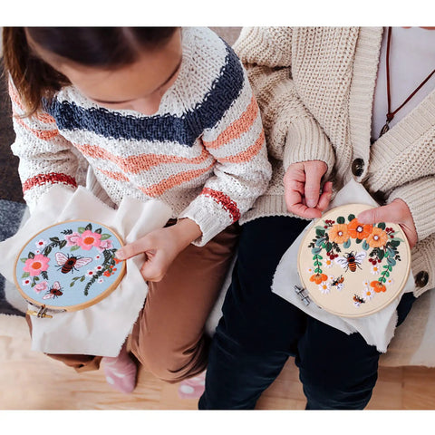 Two people using the All In One Bee Embroidery Kit For Beginners With Hoop And Thread, showcasing bee pattern cloths and threads.