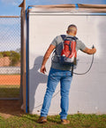 Person using Tough As Nails 18V Cordless Airless Paint Sprayer With Advanced HEA Tech on white wall outdoors.