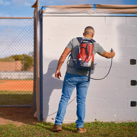 Person using Tough As Nails 18V Cordless Airless Paint Sprayer With Advanced HEA Tech on white wall outdoors.
