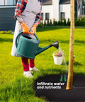 Person watering tree with 32.5 Inch Nonwoven Tree Mulch Ring Six Pack Reusable Weed Barrier Mat Degradable Go To No Fuss Weed Growth Inhibitor And Protect Tree Roots For Easy Landscape Weed Control
