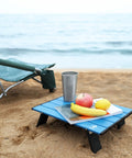 Ultralight Folding Beach Table For Camping And Picnics with food and drink on sand next to chair, 16x11x5 inch compact aluminum table