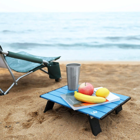 Ultralight Folding Beach Table For Camping And Picnics with food and drink on sand next to chair, 16x11x5 inch compact aluminum table