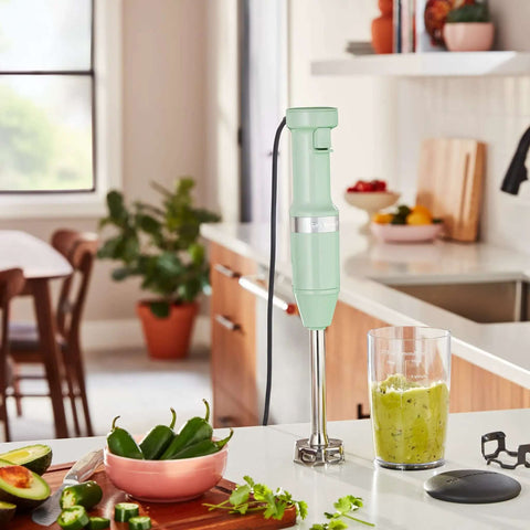 Powerful Variable Speed Corded Hand Blender With Removable 8 Inch Arm And Steel Blades For Soups And Smoothies Nifty Pan Guard Shields Cookware Pistachio immersion blender on kitchen countertop with green smoothie.