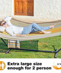 Waterproof Double Hammock With Stand For Outdoor Hangout Heavy Duty Two Person 55 Inch Quick Dry Textilene Hammock is set up on grass with a person relaxing on it, showing hardwood spreader bar and side pocket.