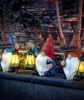 Three garden gnome statues holding shovels and solar lanterns glowing at night, on a stone ledge, waterproof resin, outdoor decor.