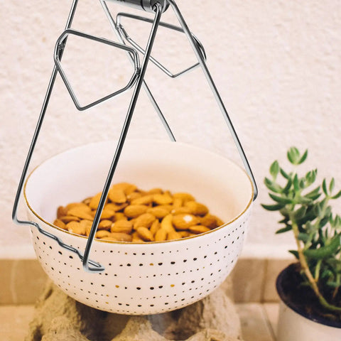 Heavy Duty No Burn Bowl Gripper Slick Stainless Steel Heat Resistant Pot Tongs lifting white bowl of almonds, non slip handle visible.