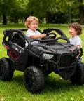 Two children in a black Powerful 24V Two Seater Ride On Car With 800W Motors, Four Wheel Drive, in a park setting