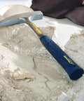 14 Oz USA Made Go To Rock Hammer With Pointed Tip And Shock Reduction Grip lying on rough stone surface.
