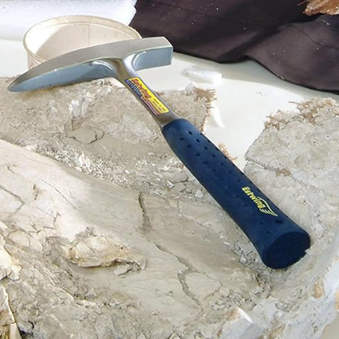 14 Oz USA Made Go To Rock Hammer With Pointed Tip And Shock Reduction Grip lying on rough stone surface.