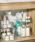 Slick Clear Under Sink Organizers And Storage Bins 2 Pack With High Low Design For Bathroom Cabinet Decluttering Pantry Organization showing stacked toiletries.