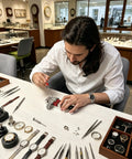 Person using a screwdriver on a watch in a jewelry store, surrounded by various watch parts and tools.