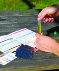 Person using ML1210 Soil Test Kit For Lawn, Garden And Potted Plants With 40 Tests, holding test tube with instructions on wooden table