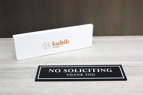 No Soliciting Sign For Front Door And Home Office, black 120 mil heavy duty, shown with Kubik Letters box on wood surface.