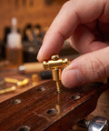 Hand holding a brass guitar roller string retainer for electric guitars, installing on headstock to fix nut noise.