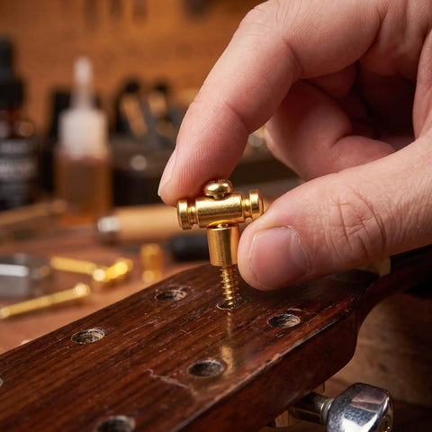 Hand holding a brass guitar roller string retainer for electric guitars, installing on headstock to fix nut noise.
