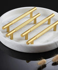 Gold cabinet handles displayed on a round marble plate with decorative elements.