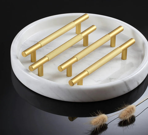 Gold cabinet handles displayed on a round marble plate with decorative elements.