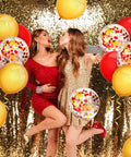 Two women in festive outfits with 80 Pcs Red And Yellow Confetti Balloons 12 Inch Party Decor For Weddings Baby Showers Birthday Parties And Events Perfect For Arch Backdrops Creating Party Vibe And Easy Decorating Supplies