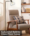 Farmhouse Bubble Glass Floor Lamp With Adjustable Tall Pole beside armchair, oil rubbed bronze finish, 6W Edison bulb, hand blown glass shade.
