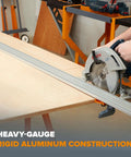 Side view of a 100-inch aluminum clamp-edge saw guide rail with T-track installed on plywood, alongside a Bosch circular saw.